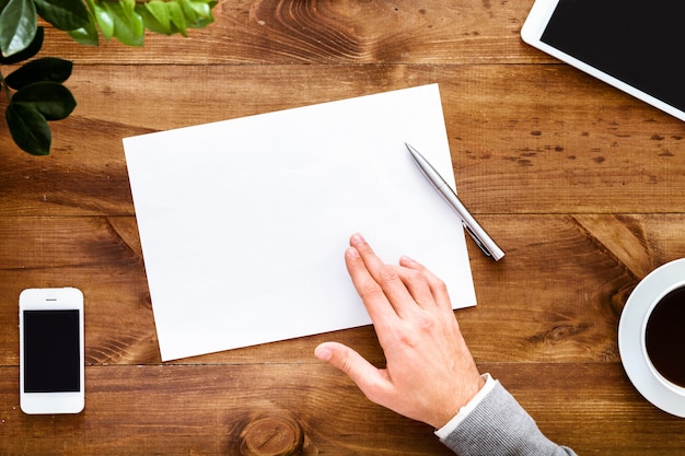 A hand writing a letter with a determined expression. The letter is placed on a desk with financial documents and a laptop in the background.