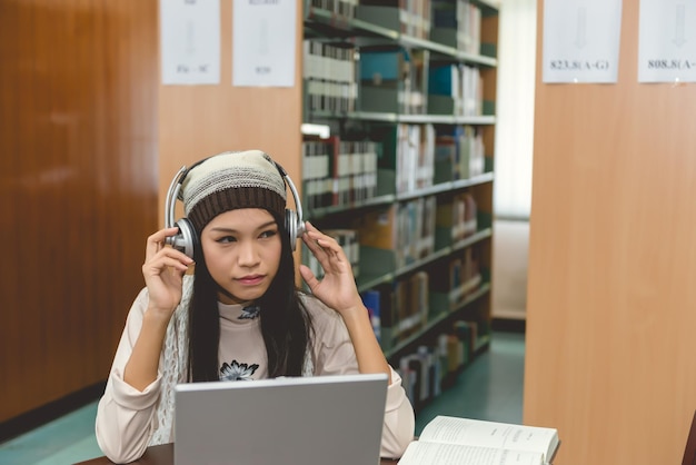 A student with a visual impairment using assistive technology in a library. The student is wearing headphones and looking at a screen with enlarged text, surrounded by books and other resources.