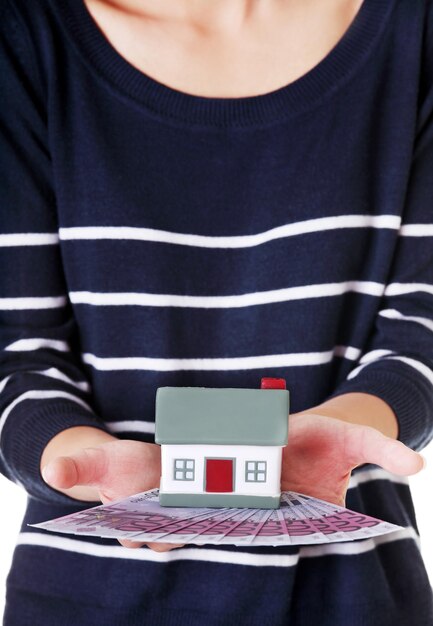 A close-up of a hand holding a miniature house overlaid with tax forms, symbolizing real estate investment and tax implications.