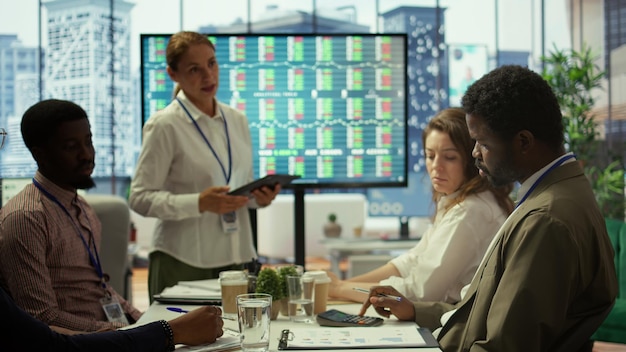 A group of diverse investors analyzing charts and reports on a large touchscreen display, showing data related to renewable energy investments, with expressions of engagement and optimism.
