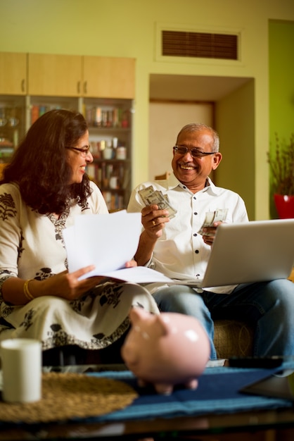 A diverse group of people around a table, some holding physical gold coins and bullion, others looking at charts on laptops, representing diverse investment strategies in gold.