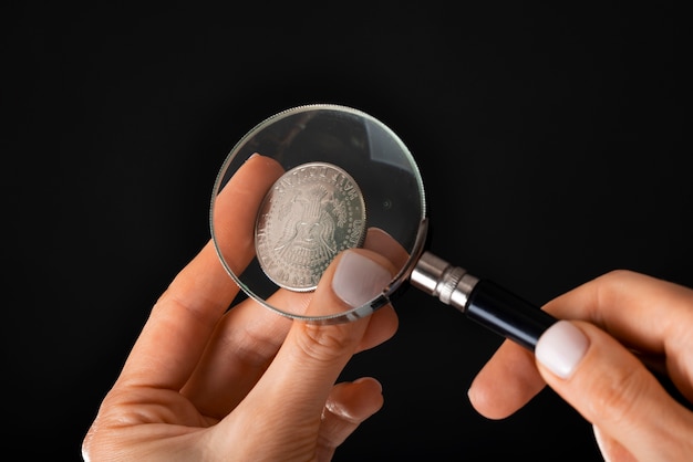 A collector carefully examining a rare coin with a magnifying glass, illustrating the importance of detailed inspection and expert appraisal in determining the value of collectibles.