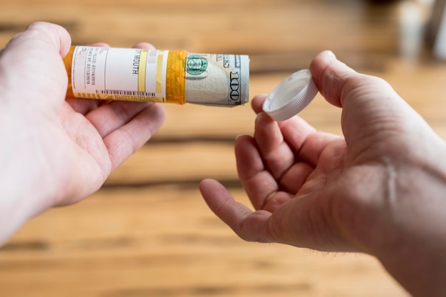 A close-up of a hand holding a prescription bottle with a dollar bill placed on top, symbolizing the high cost of medications and its impact on affordable healthcare access.
