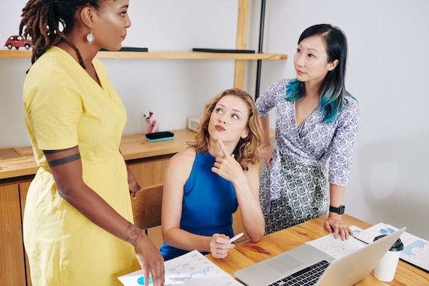 A women's business center with women collaborating around a table with laptops and notebooks, with a facilitator leading the discussion.