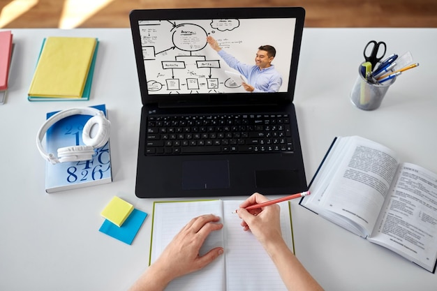 A teacher participating in a virtual professional development workshop on a laptop, with a notepad and pen nearby.