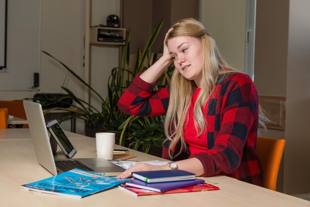 A student sitting at a desk with a laptop, looking stressed while filling out the FAFSA form. There are papers and financial documents scattered around the desk, highlighting the complexity of the financial aid application process.