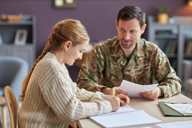 A close-up of a veteran filling out a financial aid application form at a desk, with a laptop displaying a webpage about military education benefits, symbolizing the process of accessing funding for education.