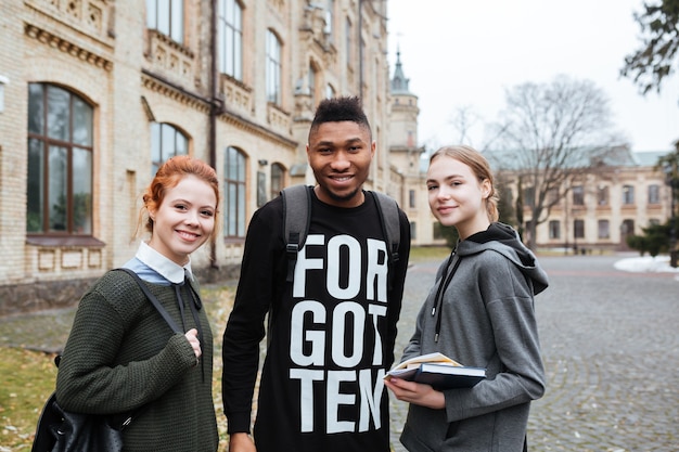 A diverse group of students stands together on a college campus, smiling and holding books. The background features a prominent university building, symbolizing access to higher education for all.
