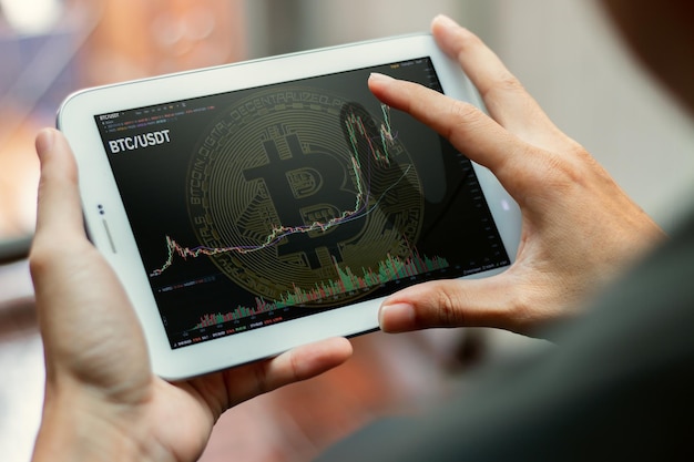 A close-up of a digital tablet showing a graph trending upwards, overlaid with Bitcoin and Ethereum logos. The background is blurred, focusing on the positive growth indicated on the screen.