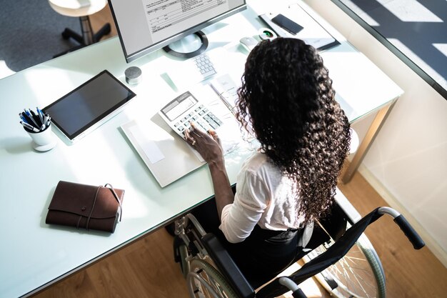 A person in a wheelchair working on a laptop, with a financial document visible on the desk, highlighting how disabled individuals can manage their finances and benefit from tax credits.