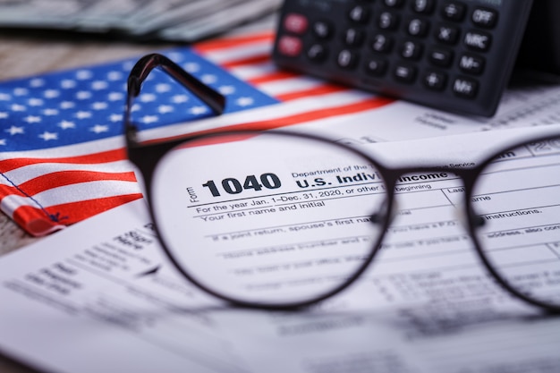 A close-up of the US tax form (1040) with a calculator, pen, and highlighting marker. The form is partially filled, showing sections related to tax credits and deductions.