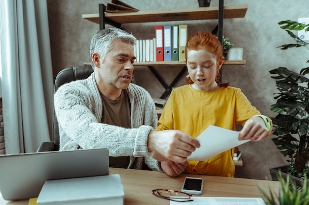 A family sitting at a table, reviewing tax documents together. The father is pointing at a form while the mother and children are listening attentively, symbolizing the process of understanding and applying for the Child Tax Credit and eligibility.