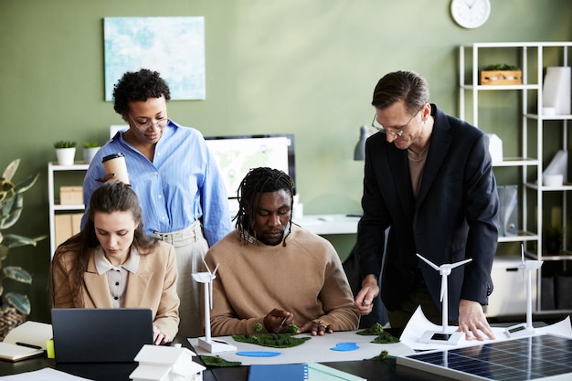 A diverse group of professionals—engineers, investors, and policymakers—collaborating on a renewable energy project. They are reviewing blueprints and discussing strategies around a conference table. The image highlights teamwork, expertise, and the collaborative effort required to succeed in the renewable energy sector.