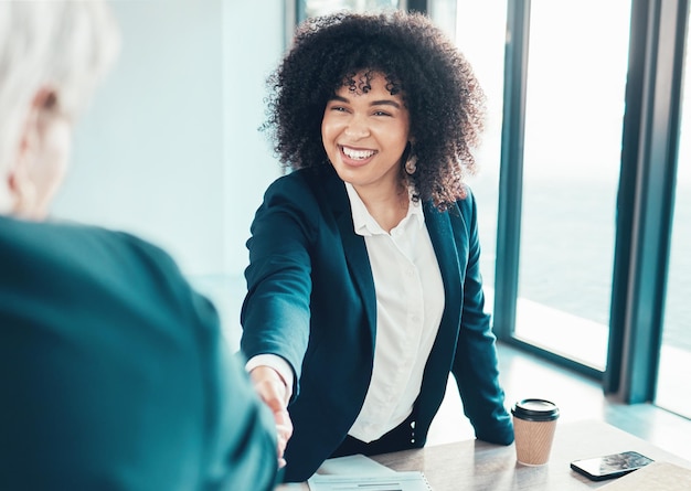 A smiling woman in a business suit shaking hands with a hiring manager in an office setting. The background shows a diverse and inclusive workplace, emphasizing the positive outcomes of job training programs.